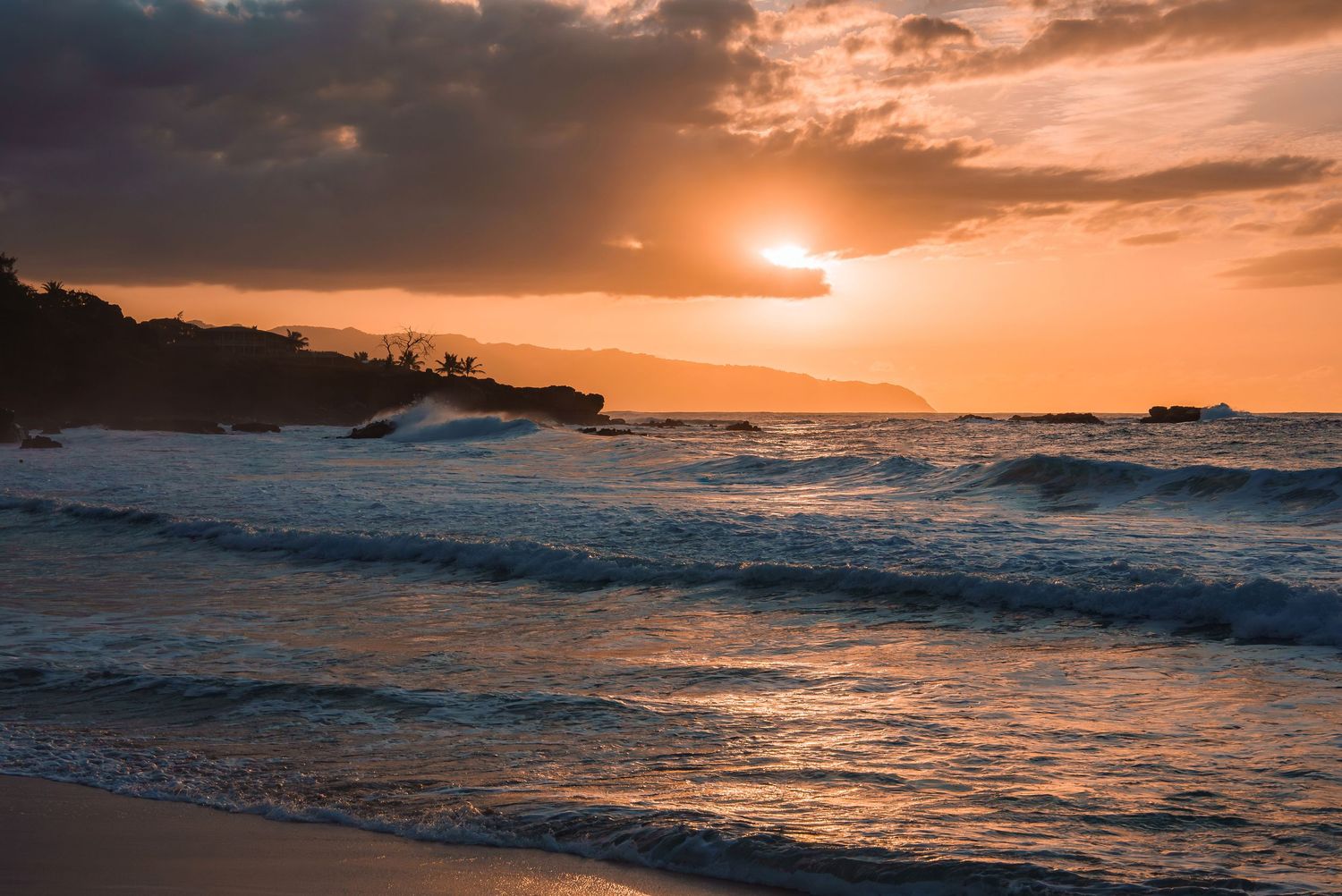 Golden sunset over the ocean with waves crashing on the shore.