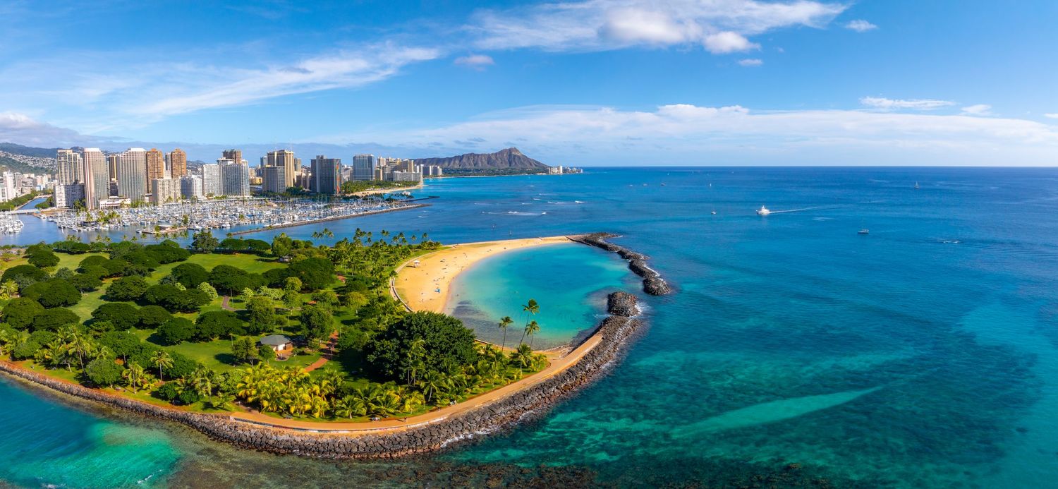 Panoramic aerial view of Waikiki Beach and Honolulu skyline with Diamond Head crater in the distance.
