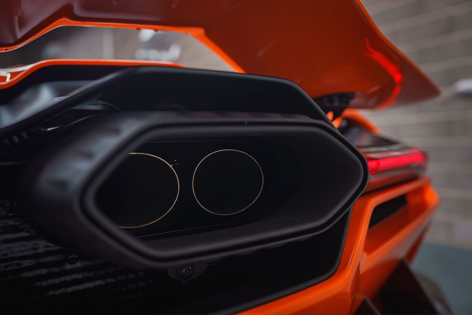 Close-up detail of dual black exhaust pipes on an orange sports car.