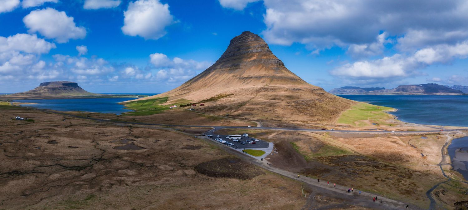 Iconic Kirkjufell mountain rises above coastal landscape in Iceland under blue skies.