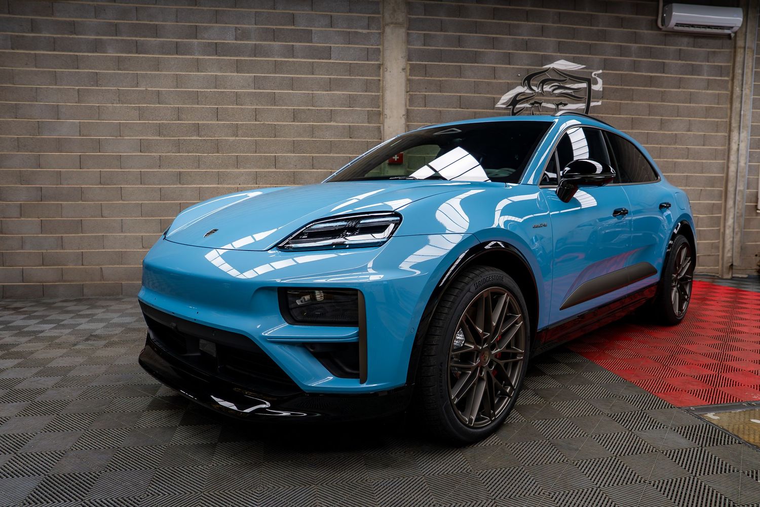 Side profile of a light blue Porsche Taycan in an indoor showroom with brick walls.