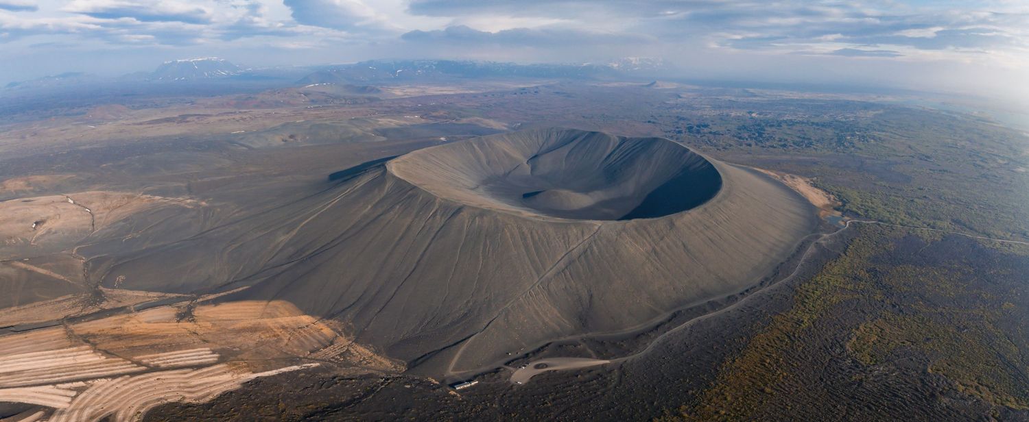 Aerial view of a volcanic crater with dark slopes against desert landscape.