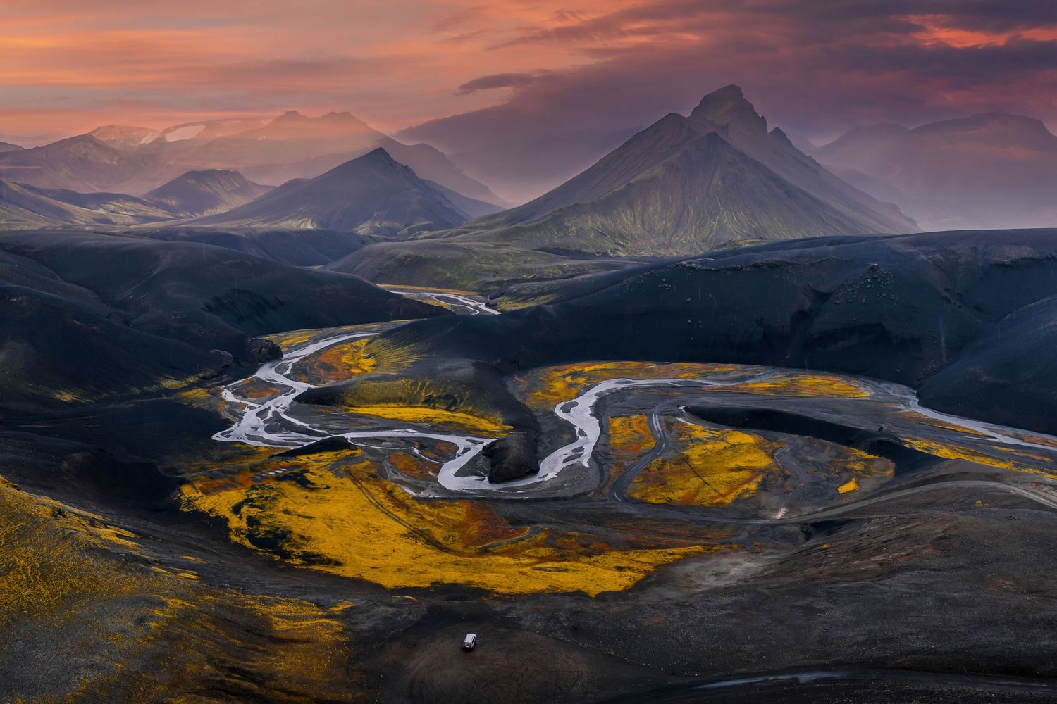 Winding river through golden valleys and mountains during dramatic sunset in Iceland's rugged landscape.