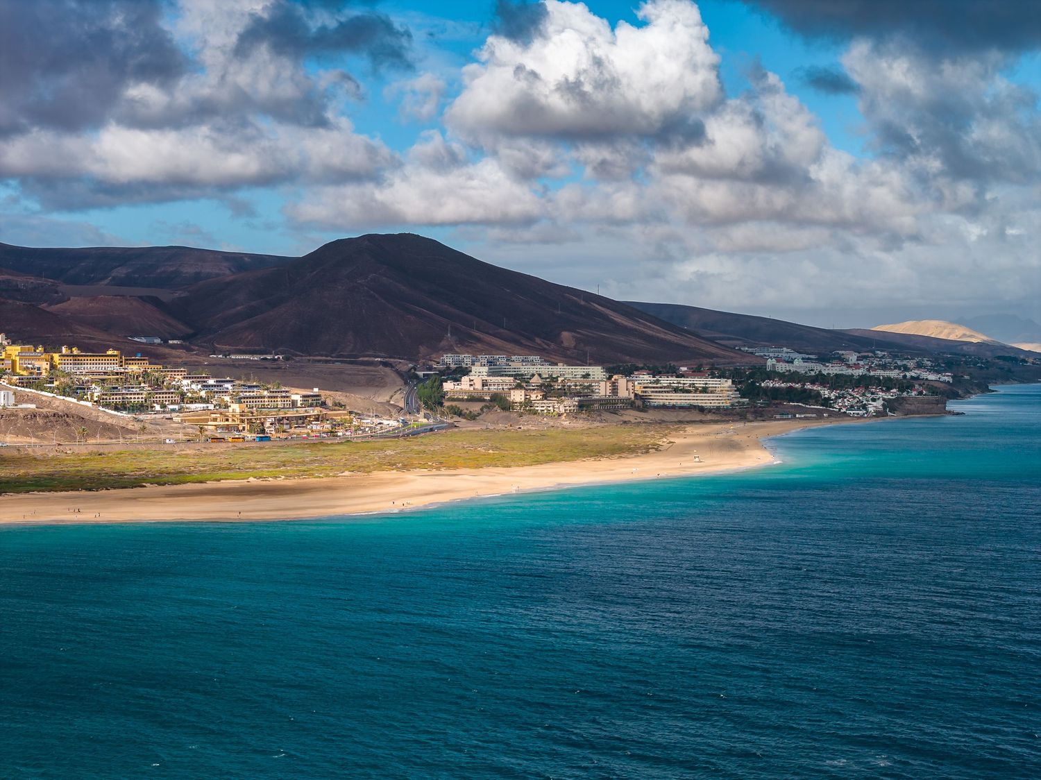 Panoramic aerial view of turquoise ocean waters and coastal mountains along Fuerteventura's scenic shoreline.