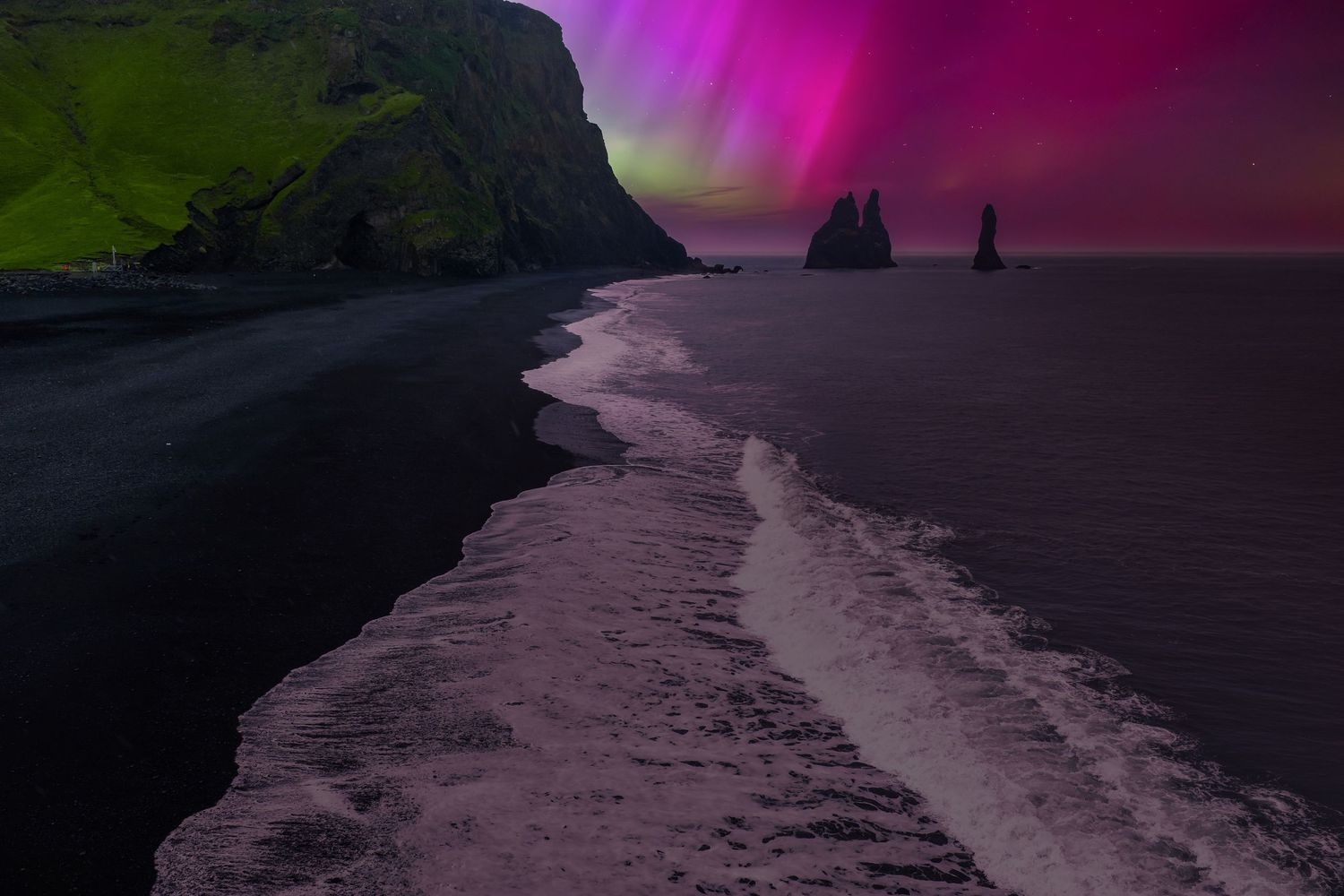 Stunning purple and pink aurora borealis dances across a dark night sky over a rocky coastline.