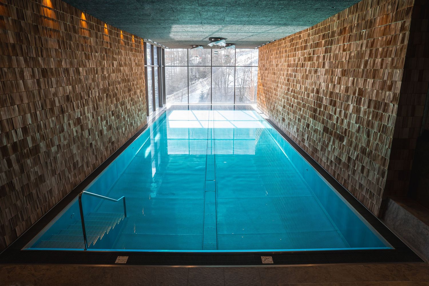 Indoor swimming pool with turquoise water surrounded by exposed brick walls and dramatic lighting.