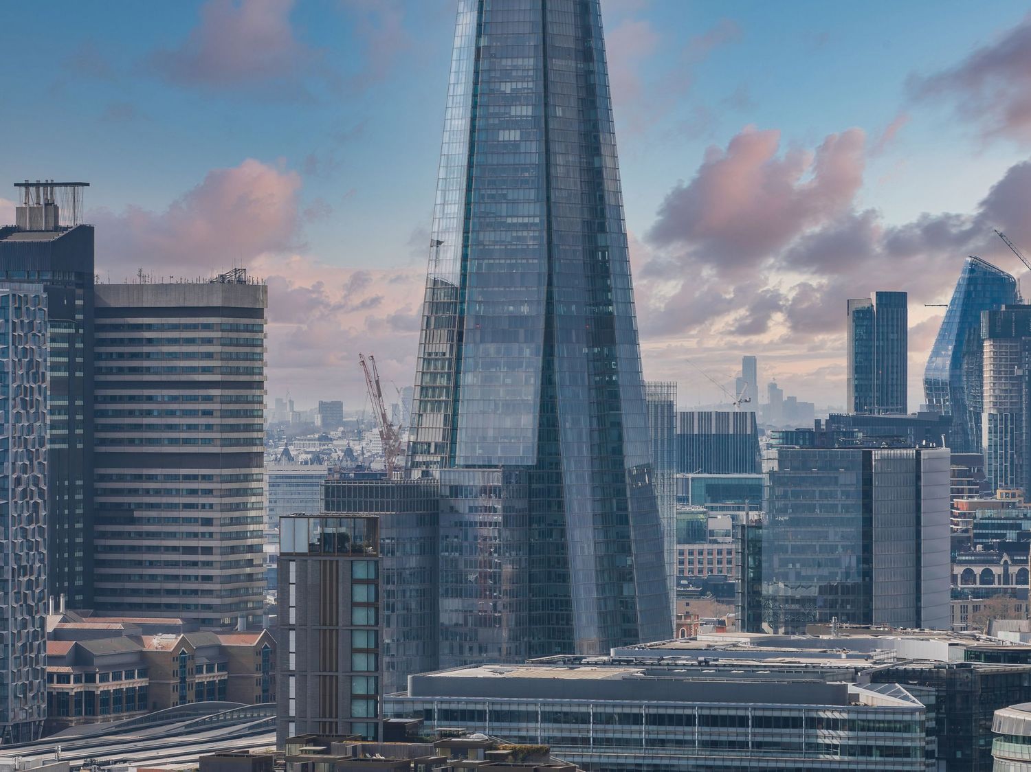 The Shard skyscraper dominates London's skyline during sunset with pink clouds.