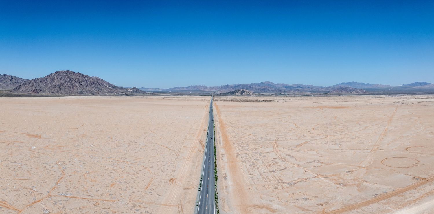 Long straight highway stretches through vast desert plains under bright blue sky.