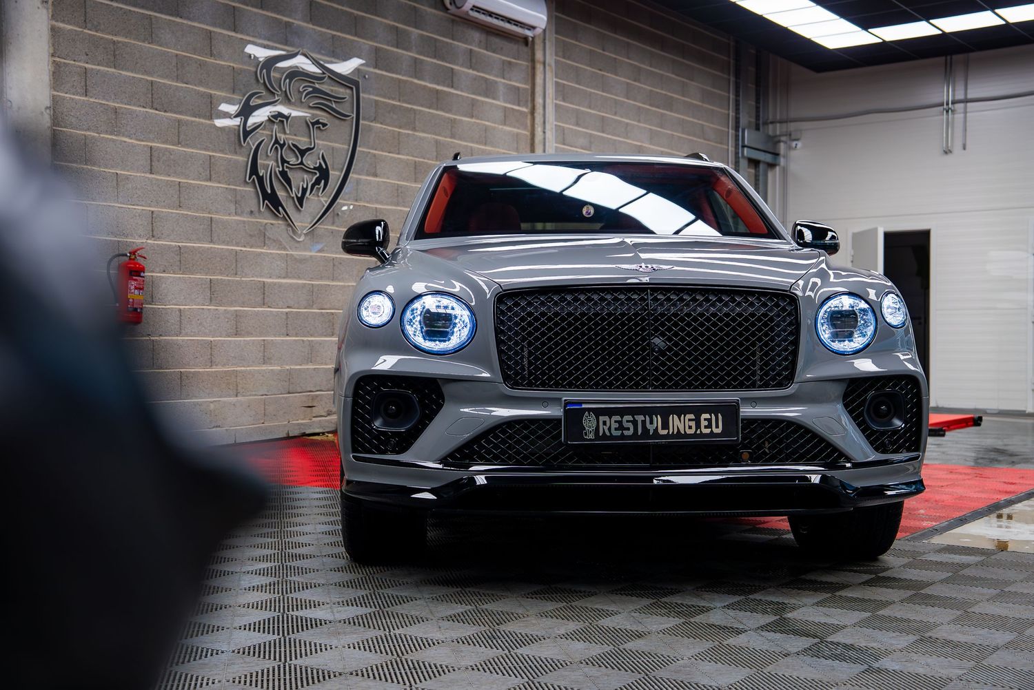 Gray Bentley Bentayga with illuminated grille and LED headlights in garage setting.