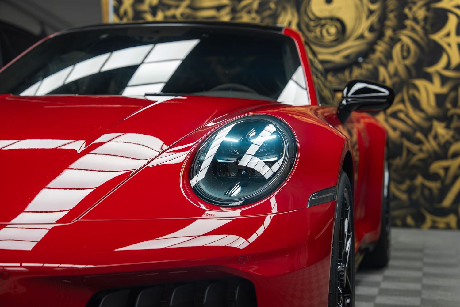Close-up view of a sleek red Porsche sports car with distinctive headlights against a decorative background.