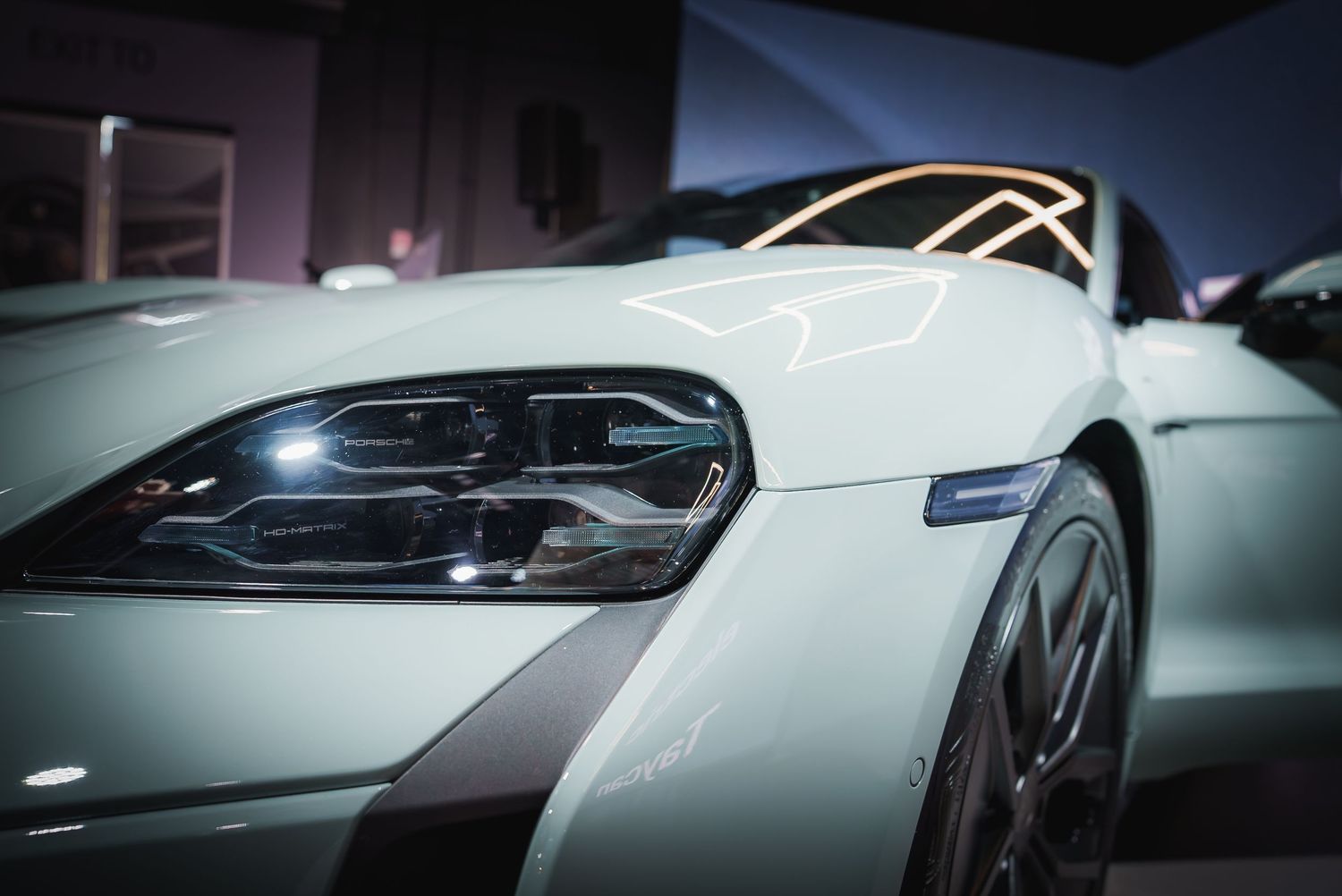 Side profile view of a white Porsche Taycan in a modern showroom with dramatic lighting.