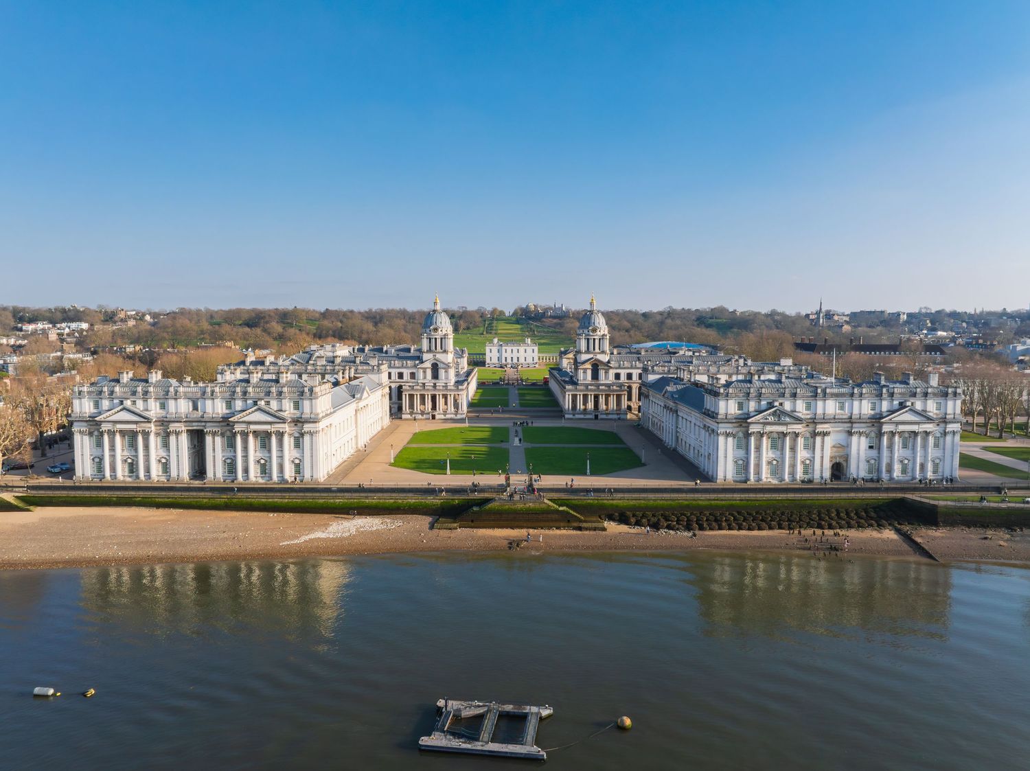 Aerial view of the symmetrical Royal Naval College buildings along the Thames River in Greenwich.