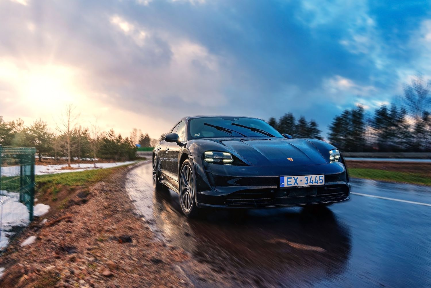 Wide-angle shot of a Porsche Taycan on a wet road during a vibrant sunset.