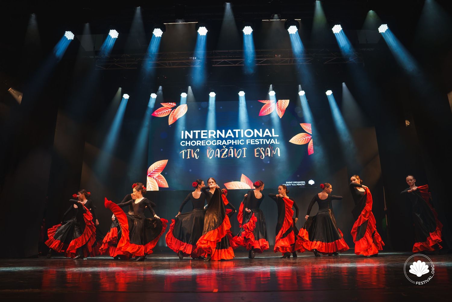 Silhouetted dancers perform under dramatic blue spotlights on a dark stage.