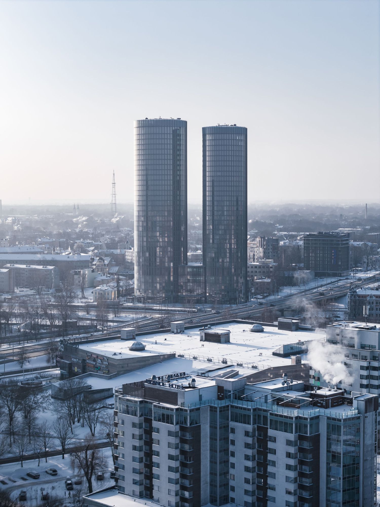 Winter cityscape with modern high-rise buildings and snow-covered rooftops in an urban setting during overcast weather.