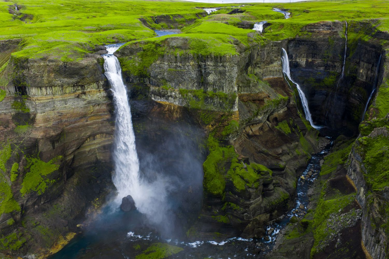 A majestic waterfall cascades down steep green cliffs in Iceland's rugged landscape during summer.