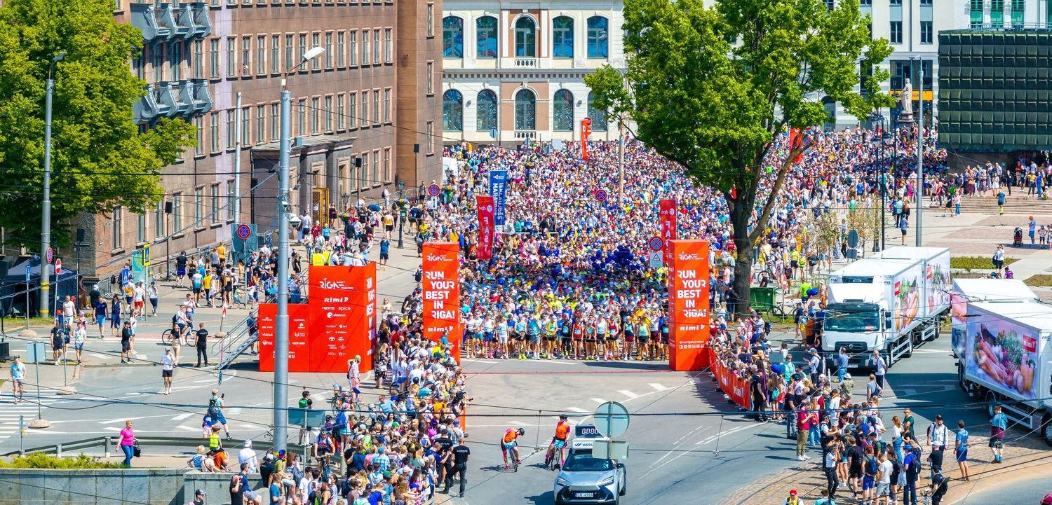 Aerial shot of crowd-lined streets with trees and urban buildings during a public event.