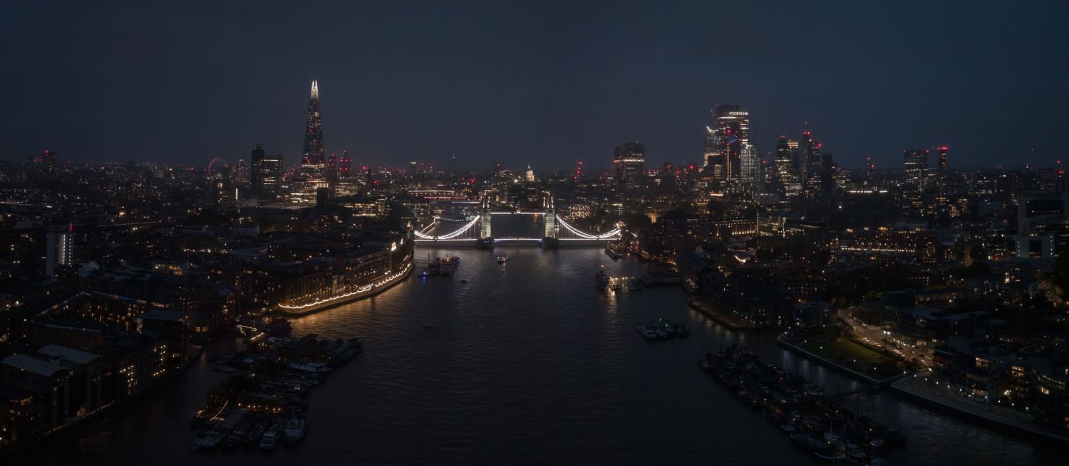 Night cityscape panorama showing illuminated buildings and bridge across water.