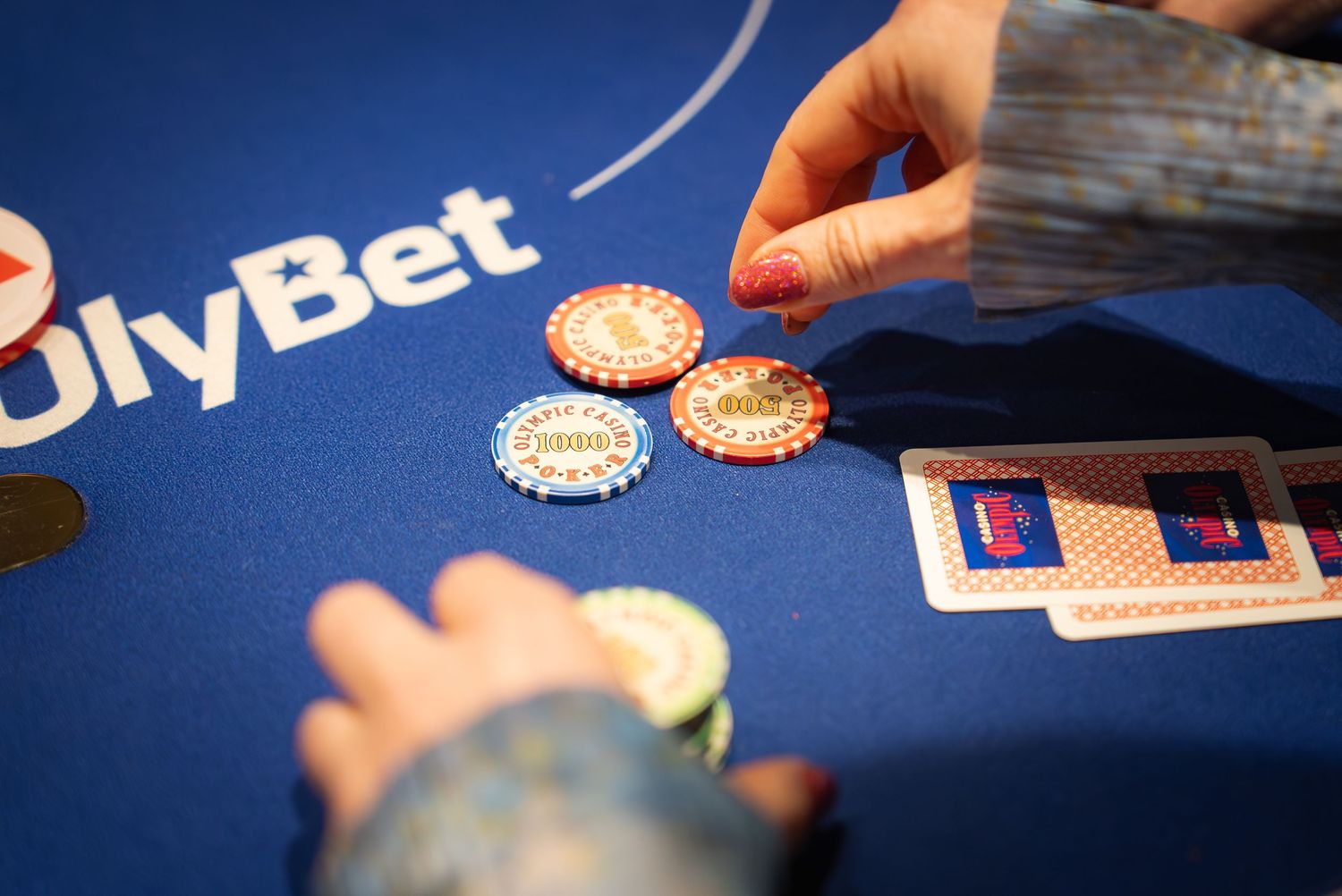 Hands moving poker chips on a blue UlyBet branded casino table.