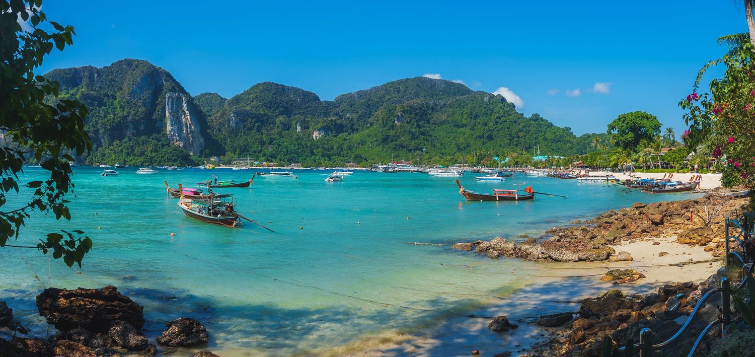 Panoramic view of tropical beach with crystal clear turquoise water and traditional boats.