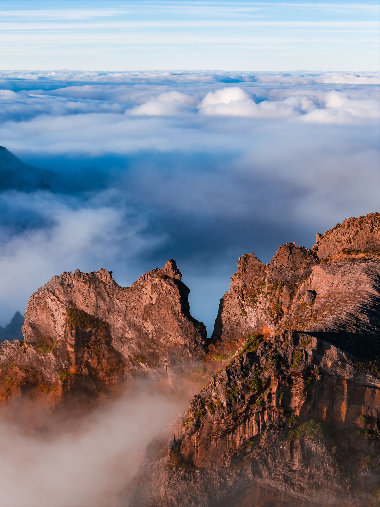 Dramatic rocky mountain peaks emerge through a sea of misty clouds during golden hour creating a mystical landscape.