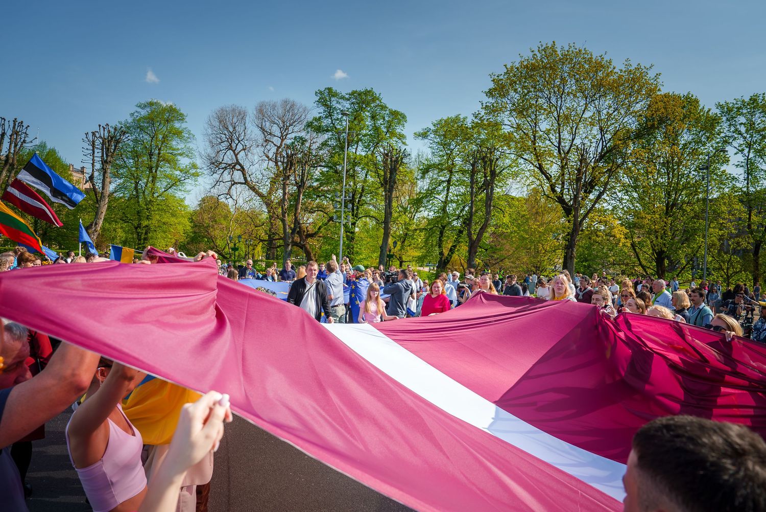 Large crowd holding pink and white banners during outdoor event.