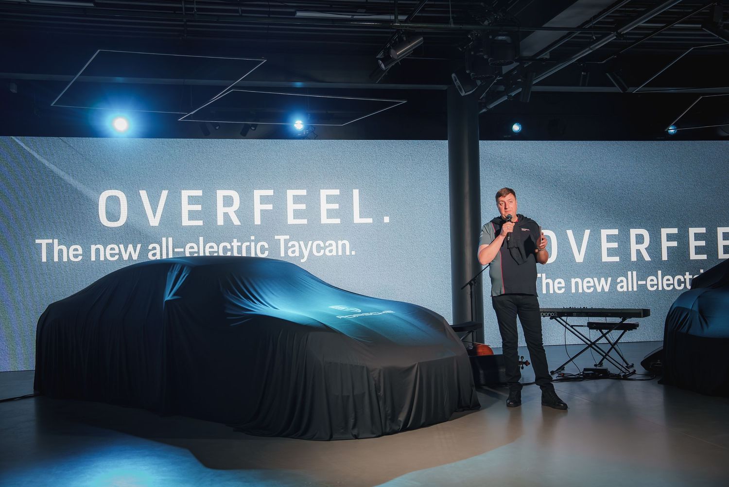 Auto show presentation stage with covered vehicle and Overfeel branding.