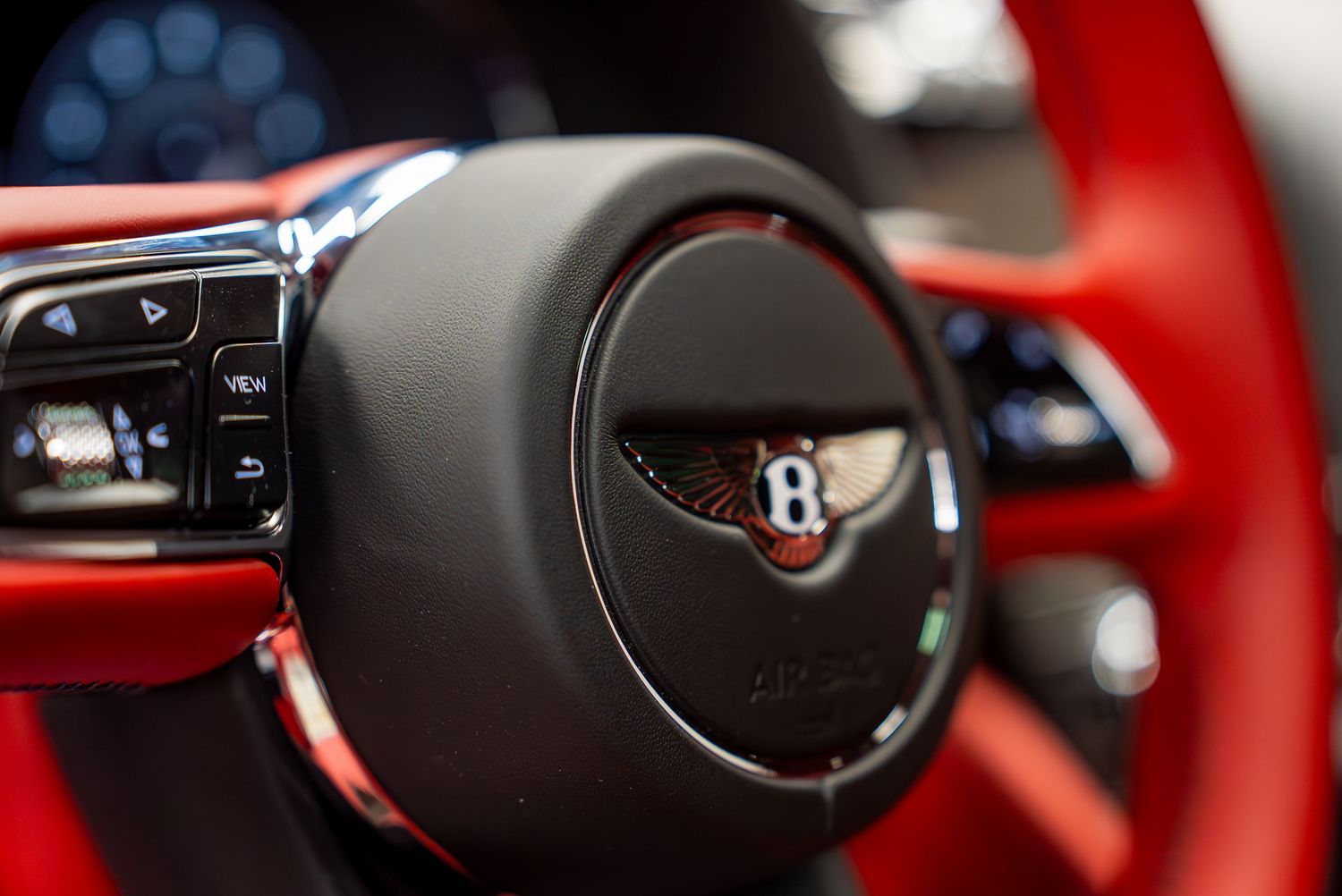 Detail shot of Bentley steering wheel controls and badge against red leather interior.