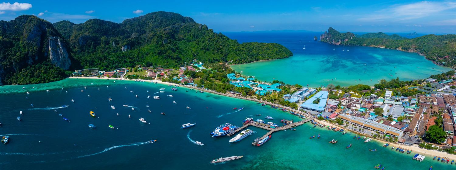 Panoramic view of a tropical bay with boats, mountains, and coastal buildings in Thailand.