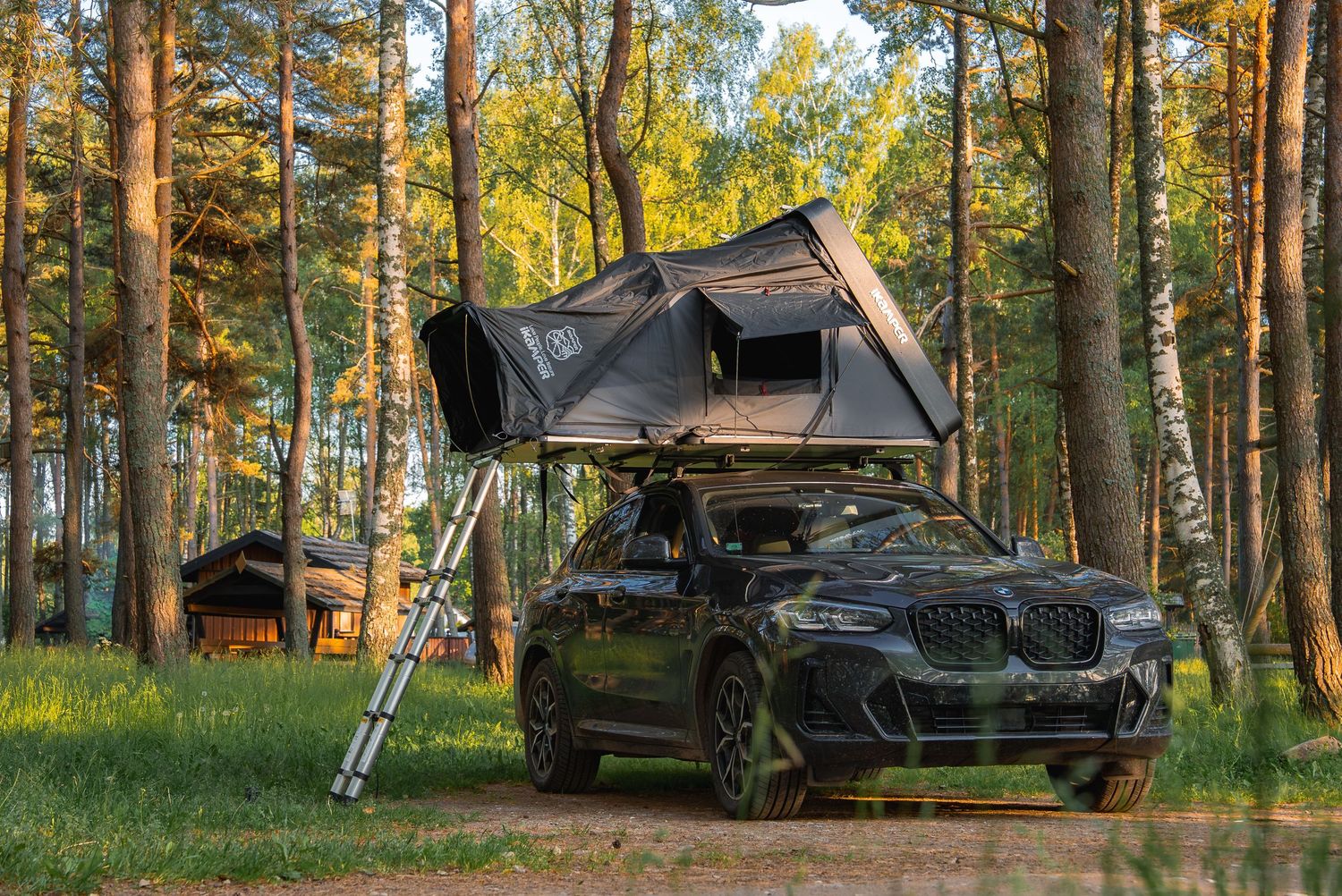 Rooftop tent camping setup on vehicle in a scenic pine forest during golden hour.