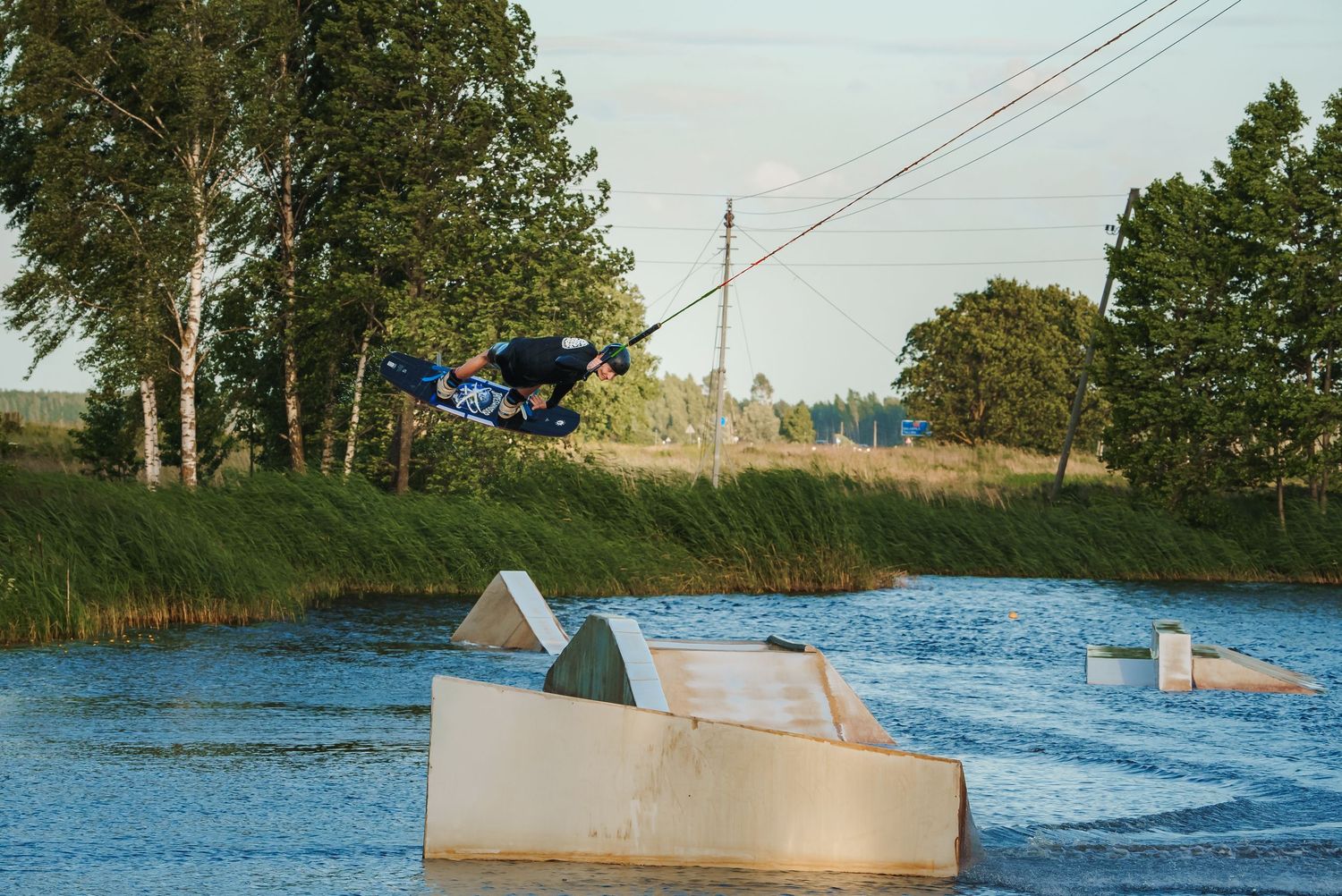 Wakeboarder executing high-flying stunt over water ramp with blue sky background.