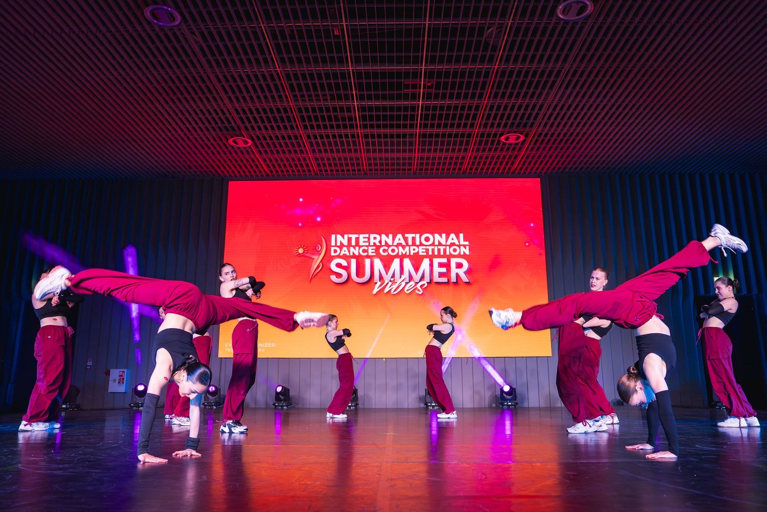 Dance ensemble performing synchronized floor movements on an illuminated stage.