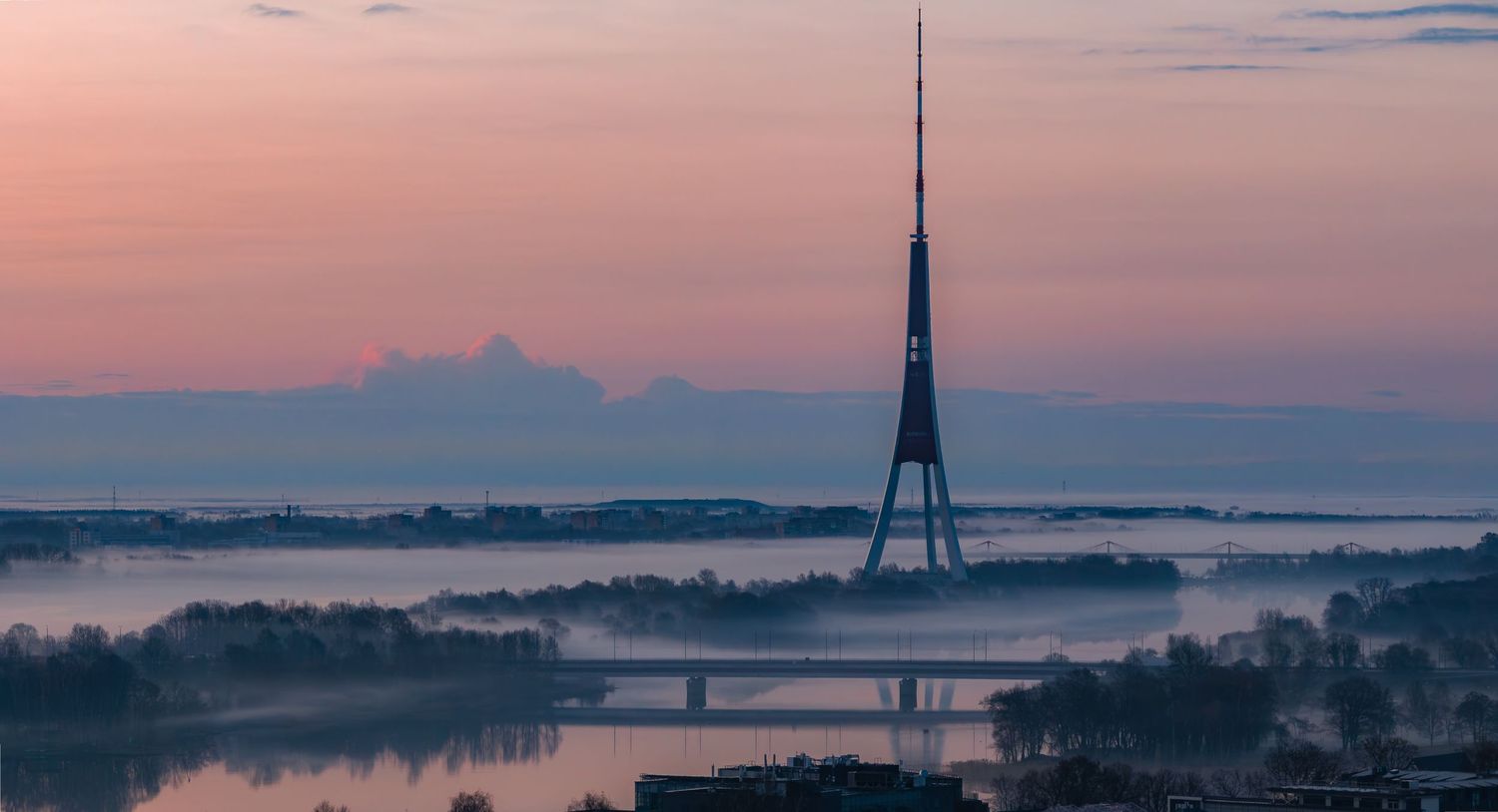 Silhouette of Riga Radio and TV Tower during pink sunset with fog rolling across the landscape.