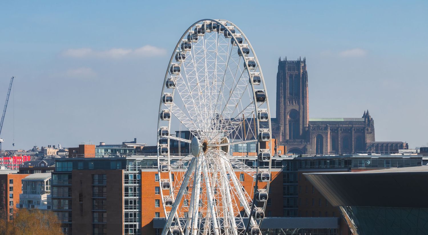 Large observation wheel against blue sky with modern city buildings in the background.
