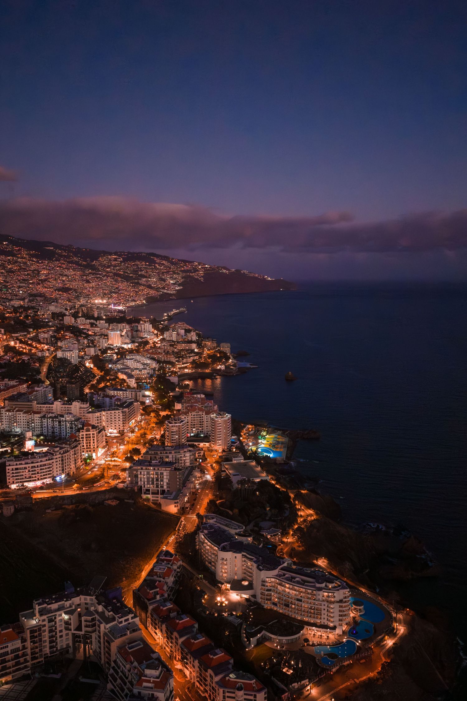 Aerial night view of Funchal, Madeira with illuminated coastal roads and buildings overlooking the Atlantic Ocean.