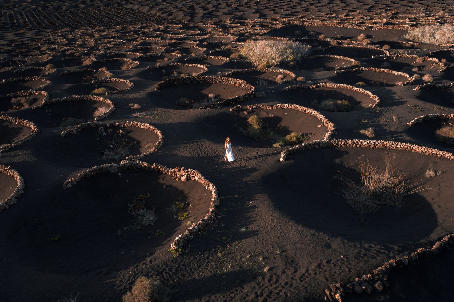 Aerial view of ancient stone terraces forming geometric patterns in a mountainous landscape at sunset.
