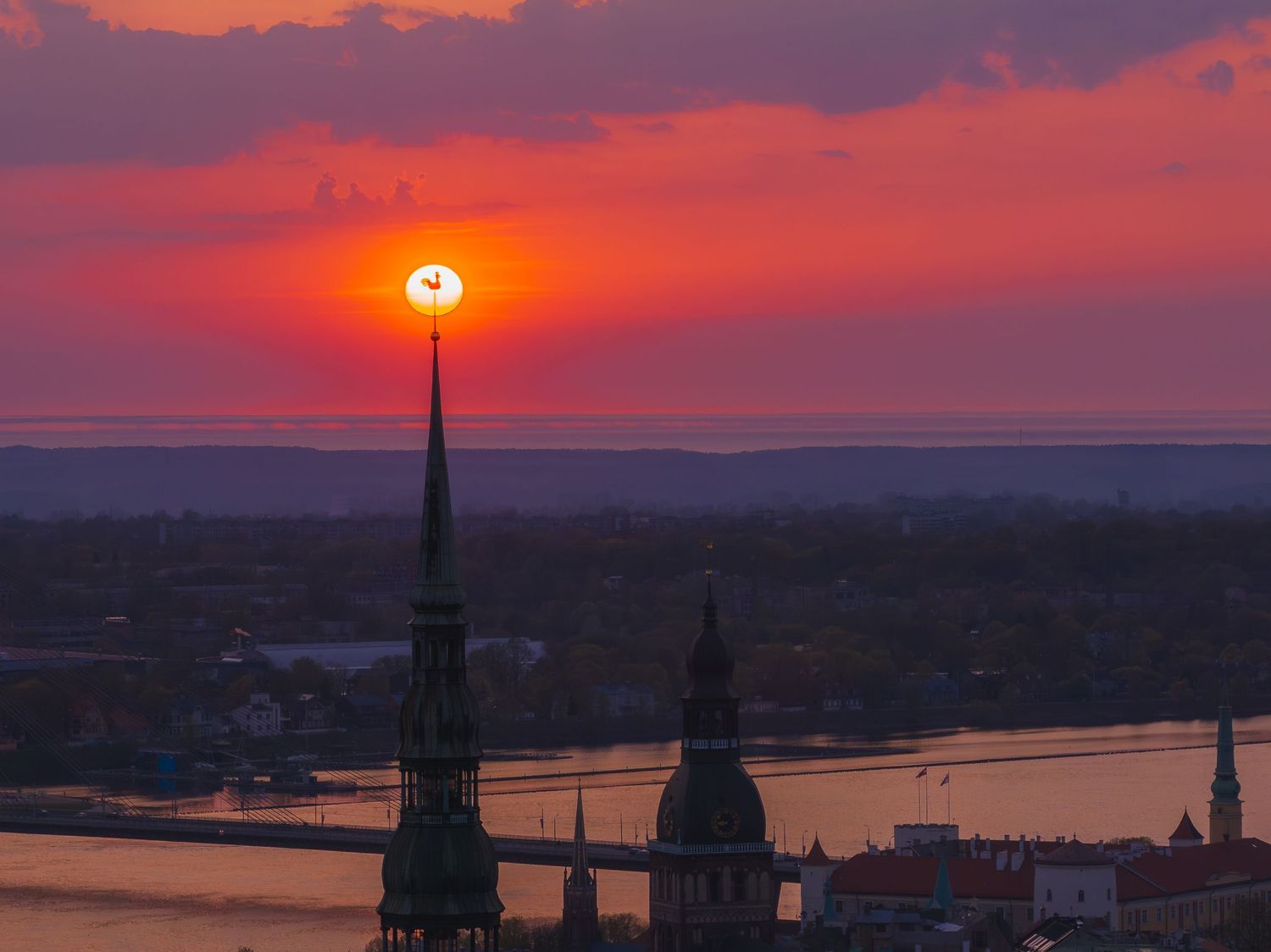 Panoramic view of a city skyline with church spires during a dramatic red sunset.