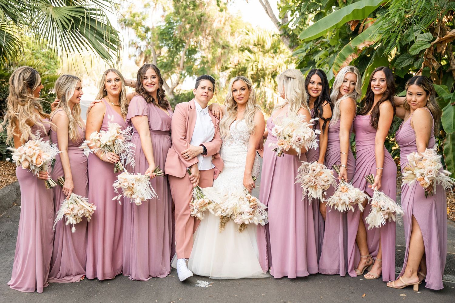Bride in the center of her bridal party, all wearing mauve pink, striking confident, sassy poses with palm trees in the botanic garden.