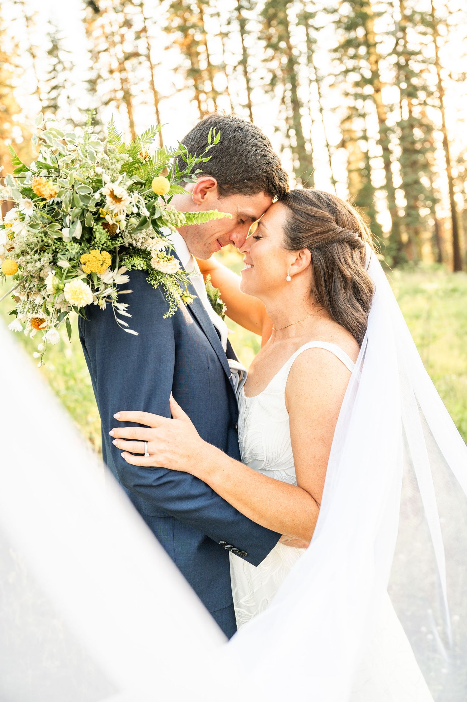 Close-up of bride and groom during sunset photos at Sugar Bowl Ski Resort, with trees in the background and the sun peeking through.