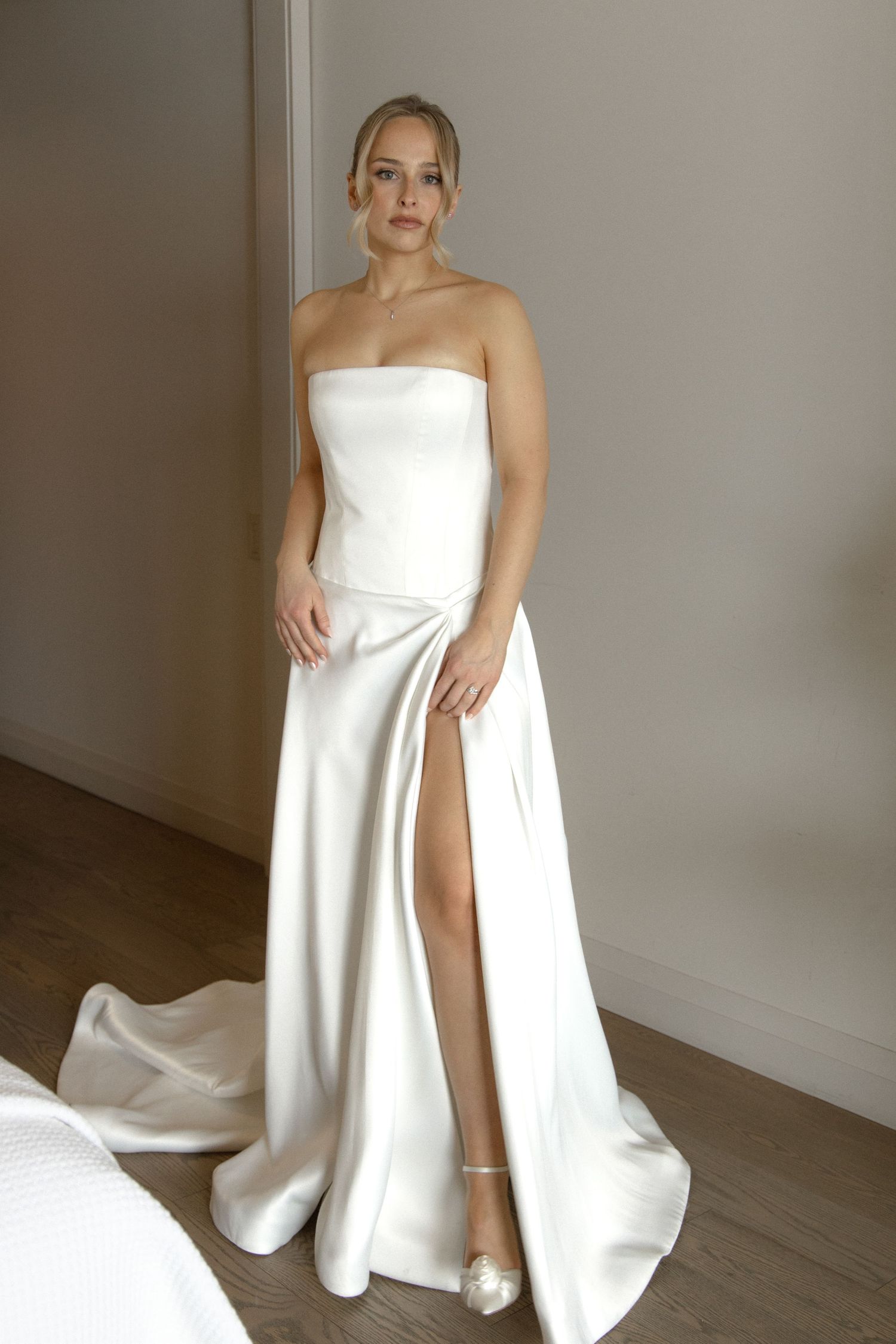 Elegant bride in minimalist strapless white satin wedding gown with high slit and train.