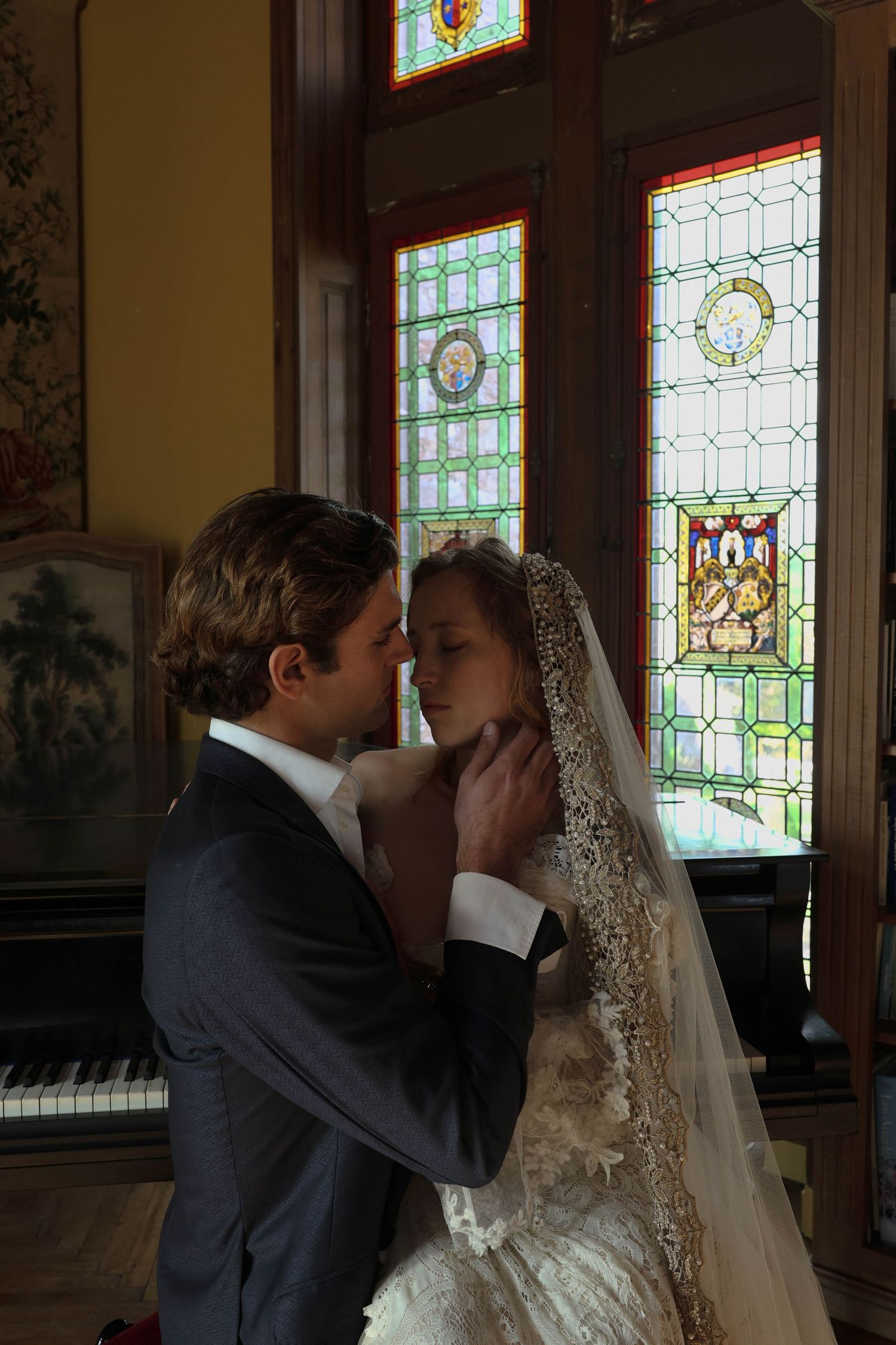 Groom tenderly holding brides face near stained glass window during intimate wedding ceremony moment.