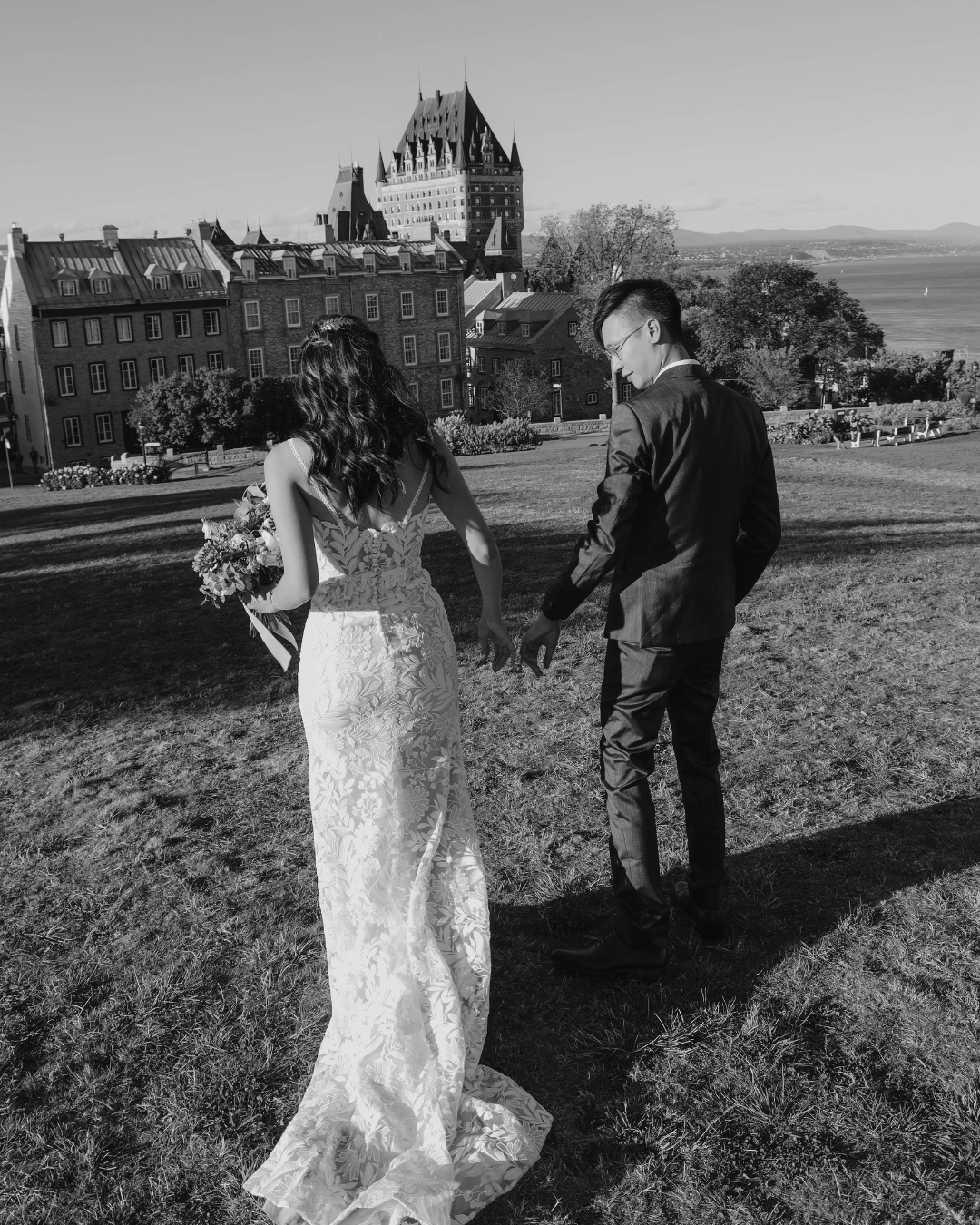 Black and white photo of bride and groom holding hands facing Chateau Frontenac in Quebec City.