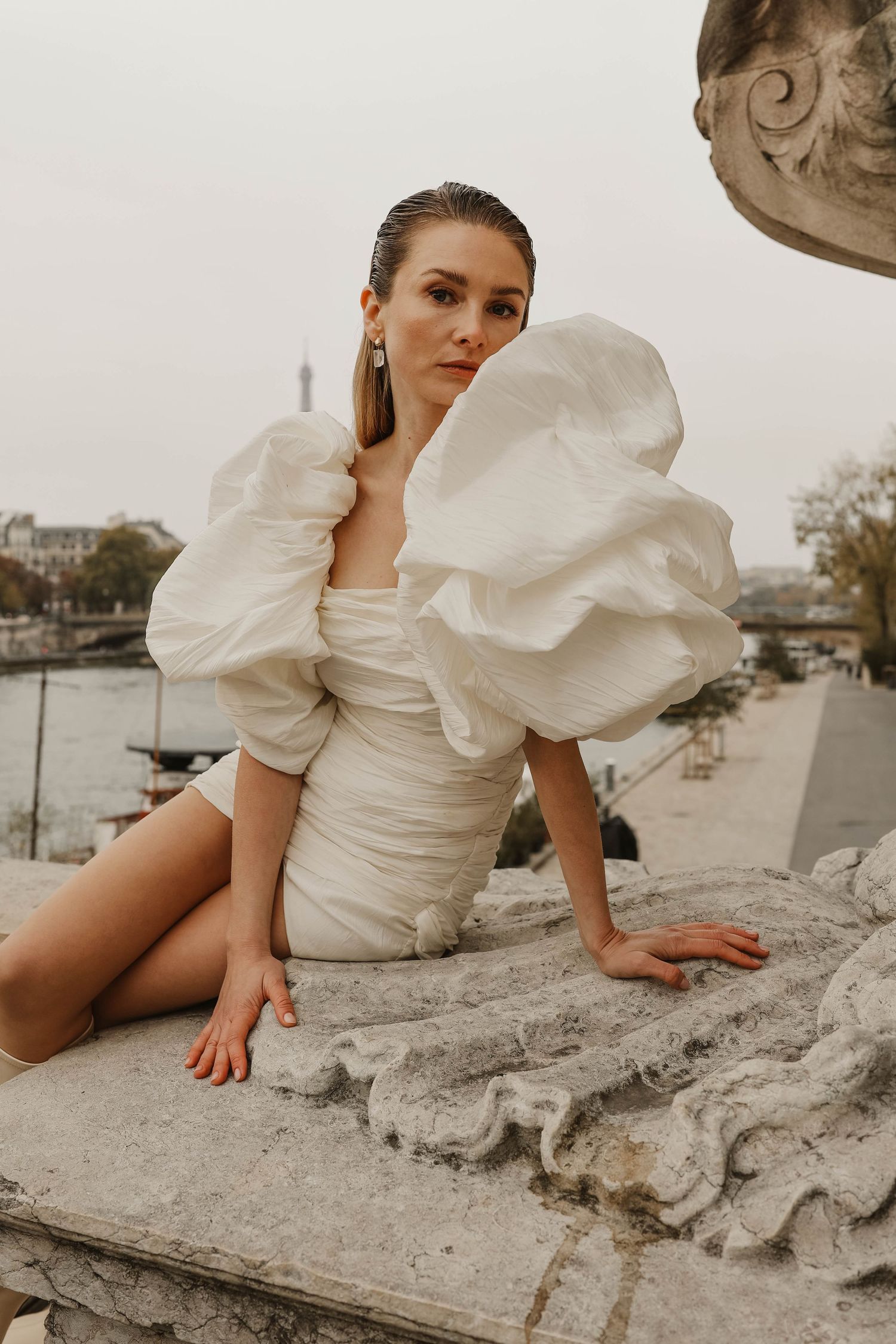 Woman in white mini puff-sleeve bridal dress seated on stone balcony with Eiffel Tower in background.