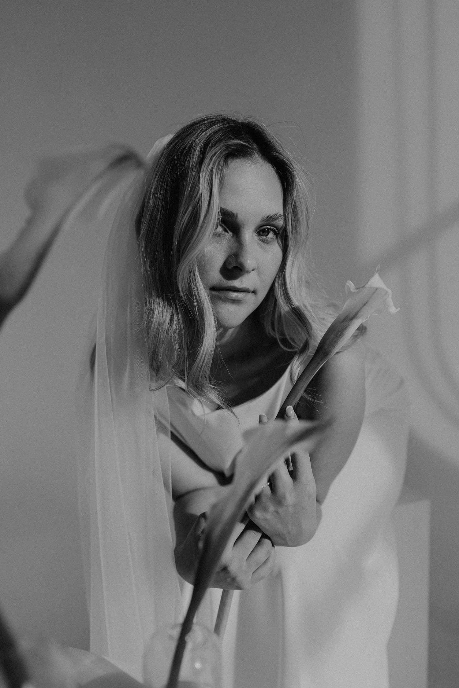 Black and white portrait of a blonde bride holding calla lilies with a flowing veil.