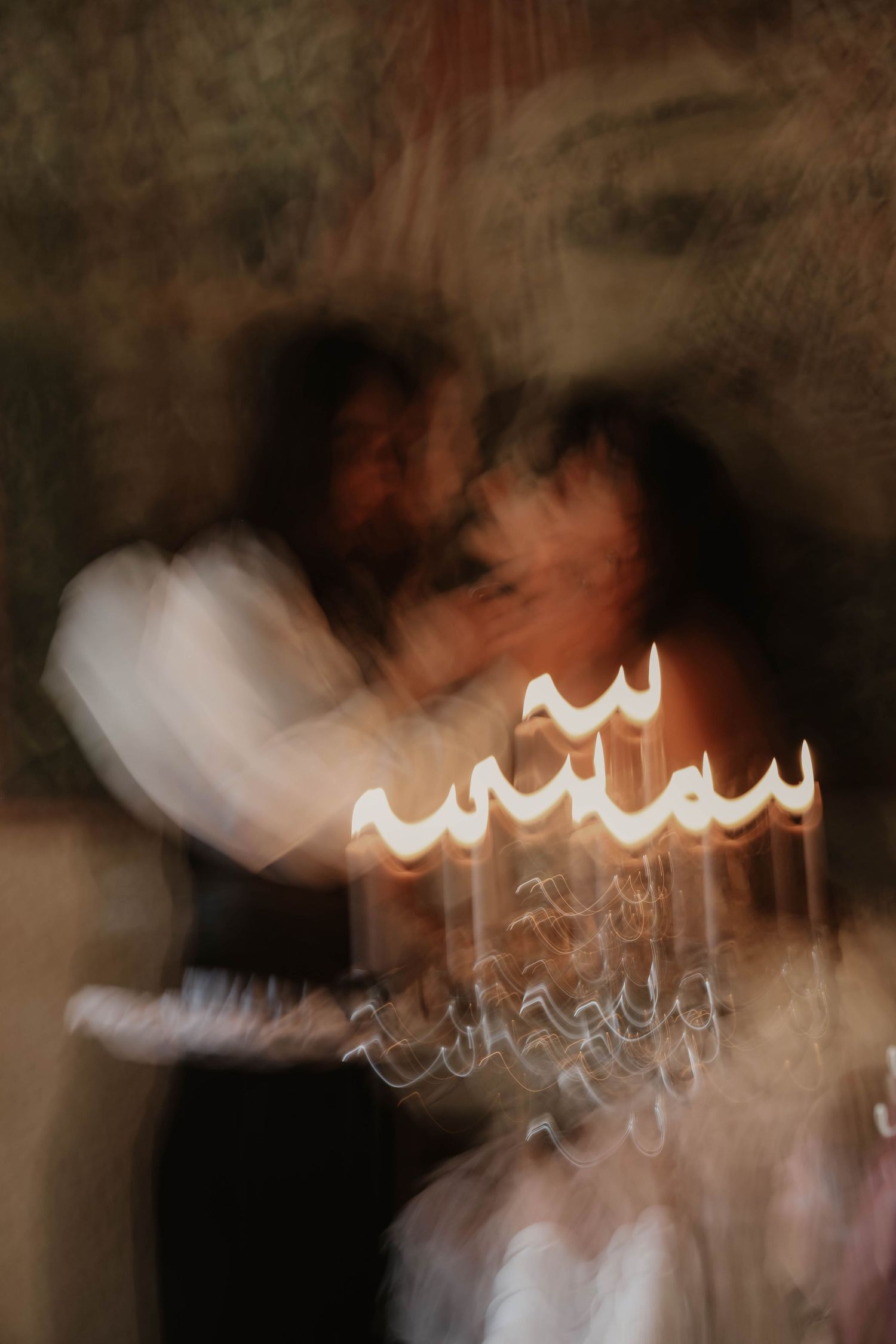 Artistic motion blur photo of couple kissing near glowing candelabra at wedding.