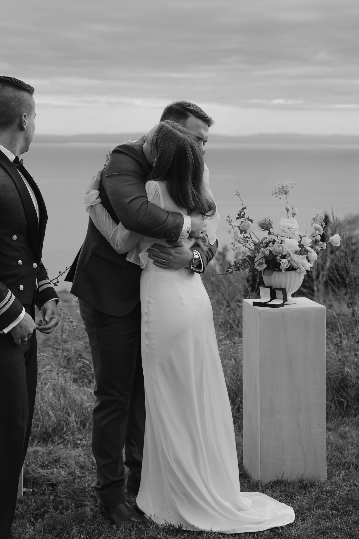 Black and white photo of couple sharing first kiss at outdoor cliff wedding ceremony by the ocean.