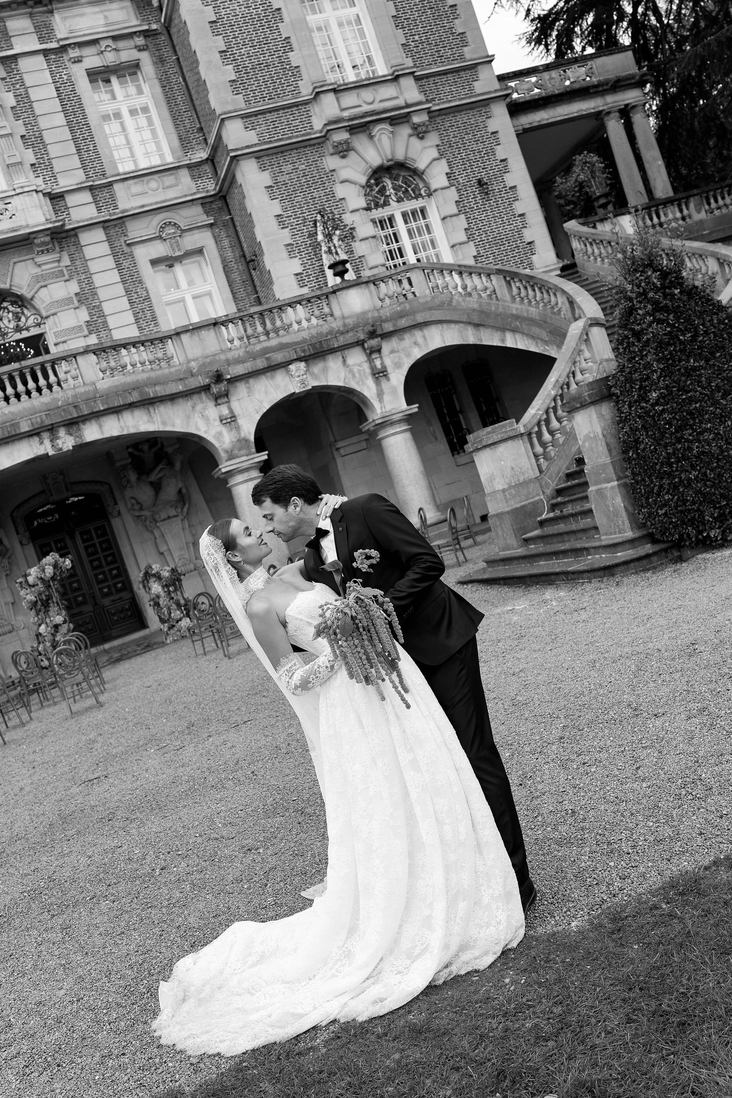 Romantic black and white photo of bride and groom sharing a kiss outside a grand French chateau.