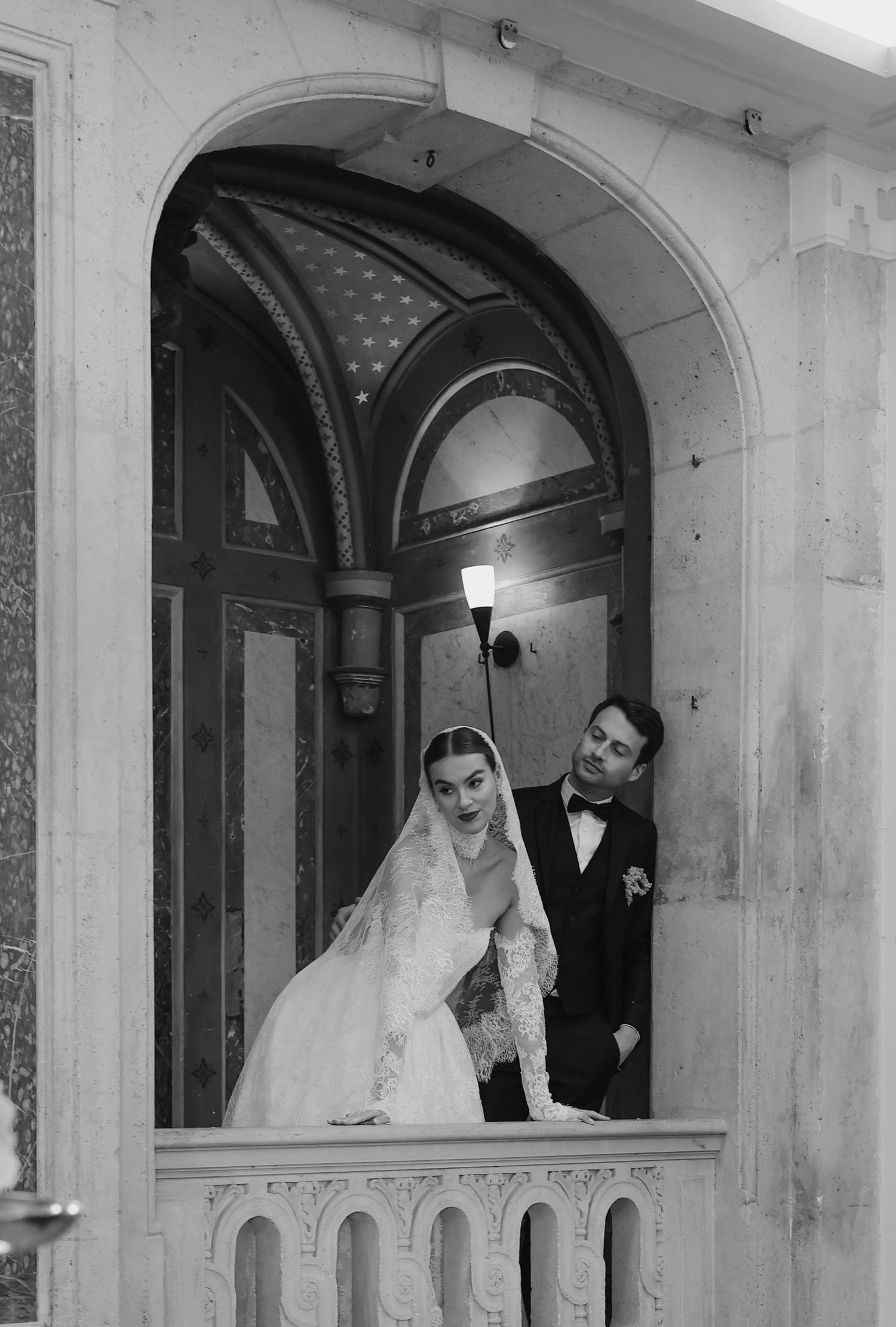 Elegant bride and groom standing in an ornate marble archway in a classic black and white wedding portrait.