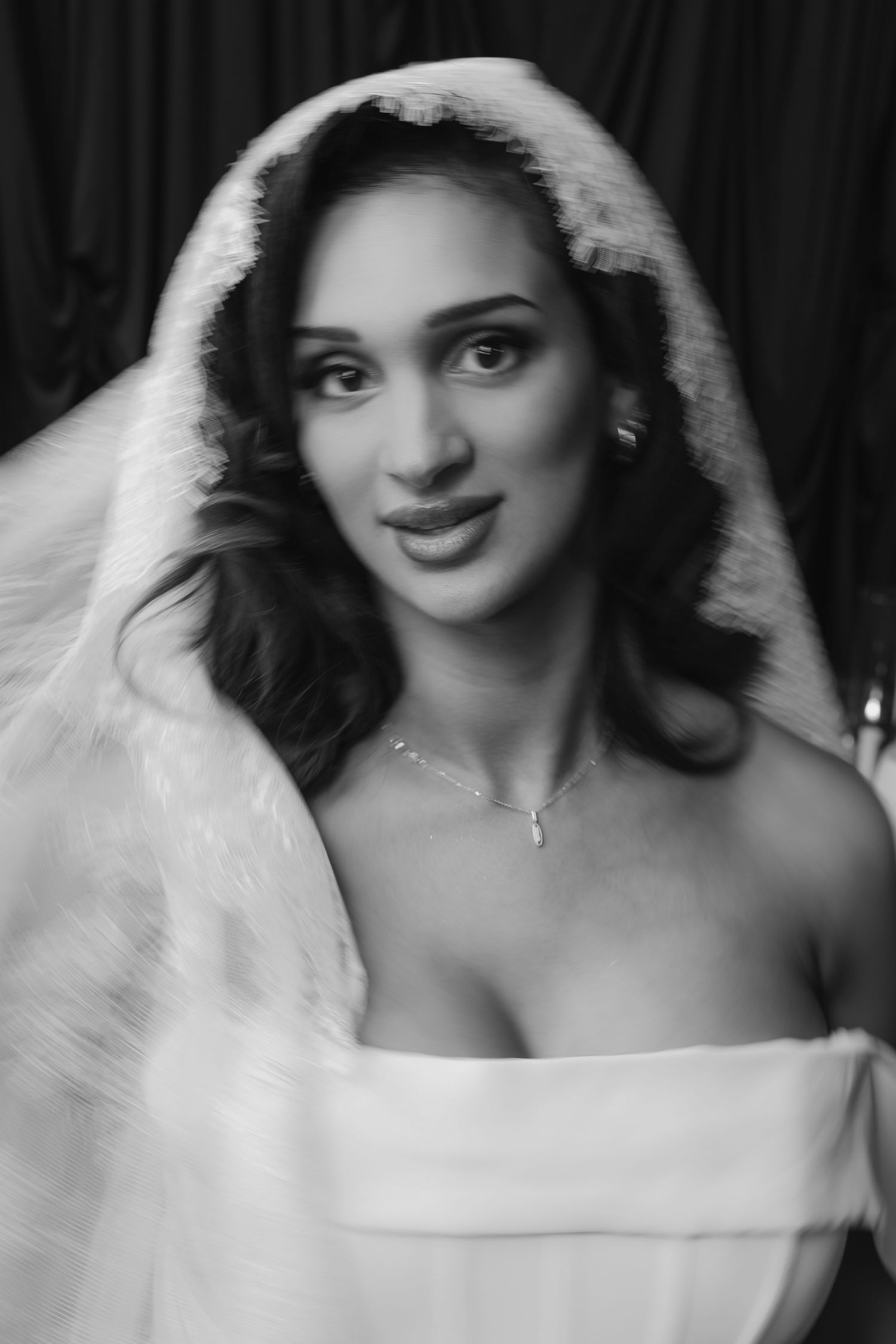Black and white portrait of a bride wearing a veil and strapless gown with a delicate necklace, smiling softly.