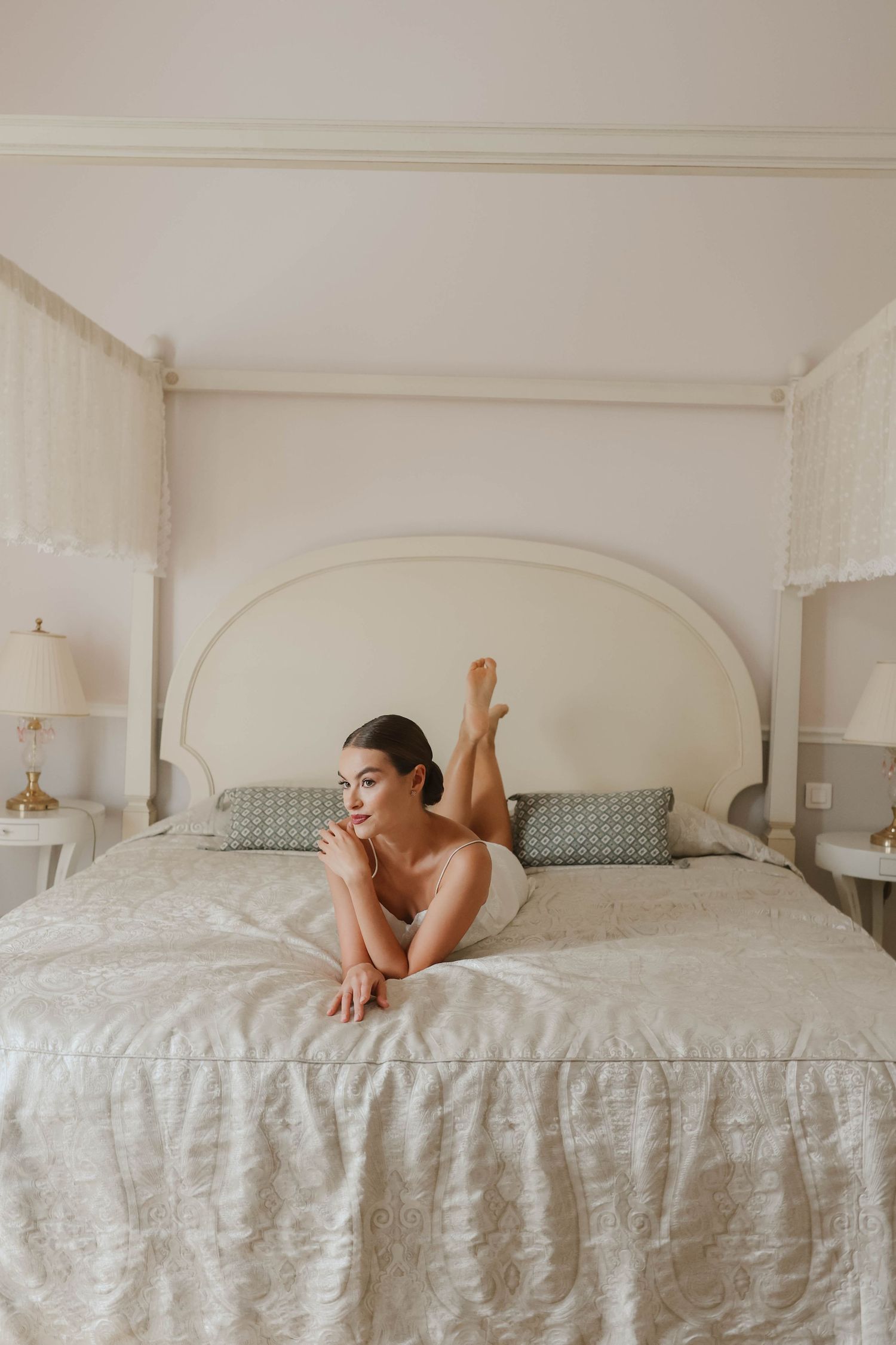 Beautiful bride in white lingerie posing gracefully on a luxurious four-poster bed in an elegant room.